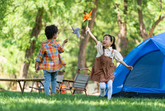 两个小孩子在草地上举着风车开心奔跑