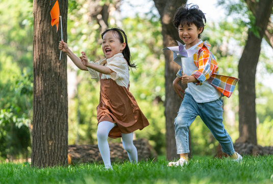 两个小孩子在草地上举着风车开心奔跑