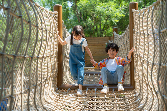 两个小孩子相互鼓励牵手走绳桥