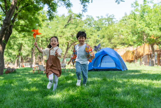 两个小孩子在草地上举着风车开心奔跑