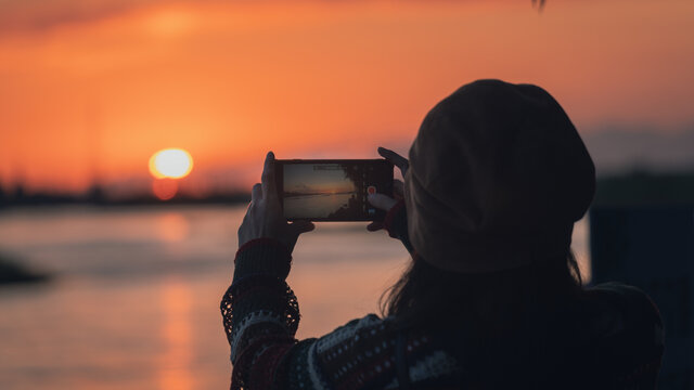 夕阳下拿手机拍照的女孩