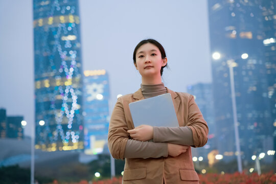 在办公楼外职业女性抱着电脑行走