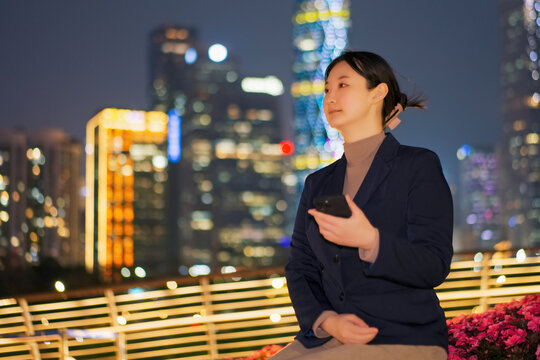 在夜晚城市桥上手拿手机的女性