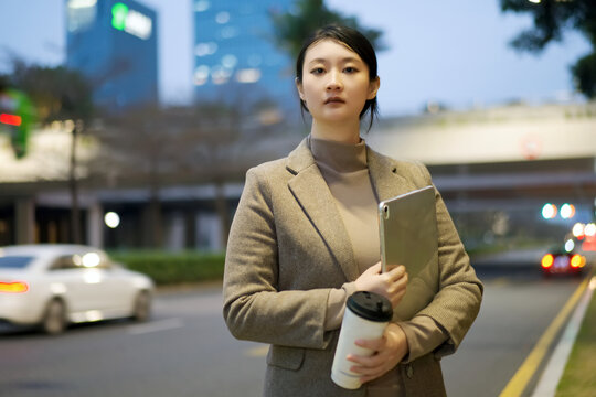 自信女性手拿电脑走在傍晚街道上