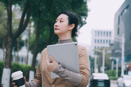 自信女性手持电脑茶歇走在街道上