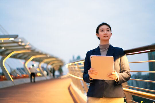 在夜晚城市桥上自信女性手持电脑