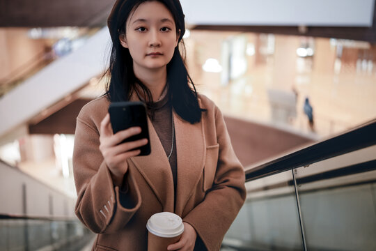 年轻女性在商场扶梯上喝咖啡