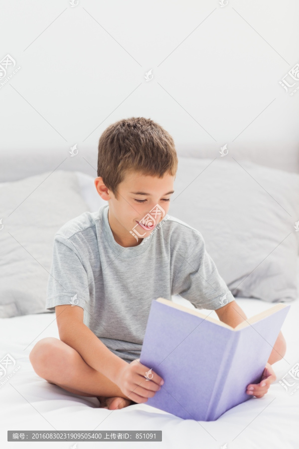 小男孩坐在家里的床上看书