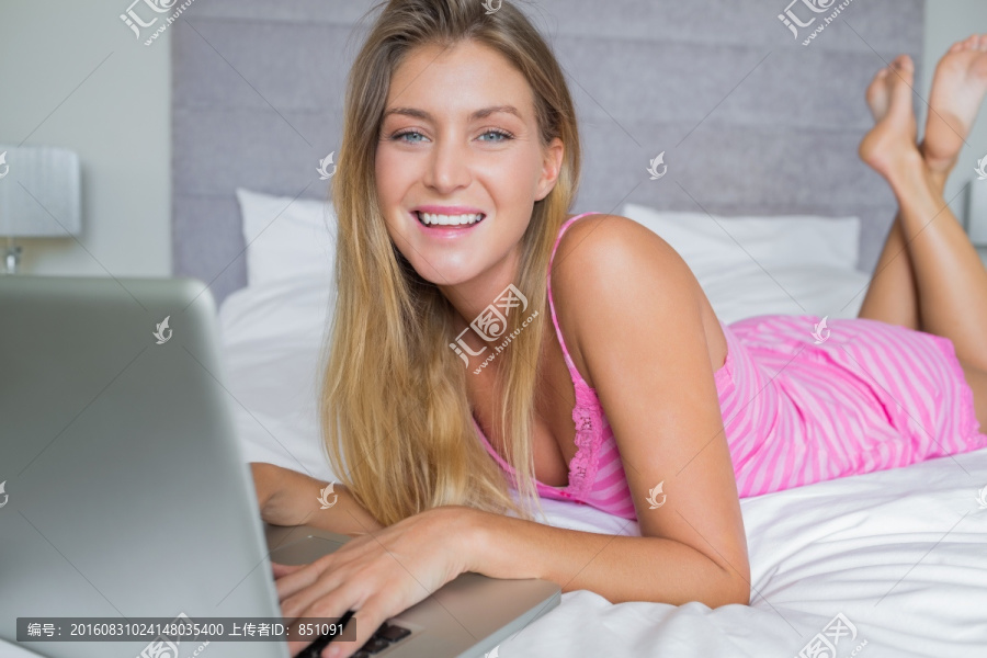 金发女郎趴在床上用笔记本电脑