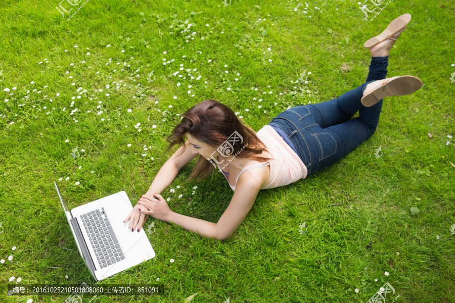 女子趴在草地上使用笔记本电脑