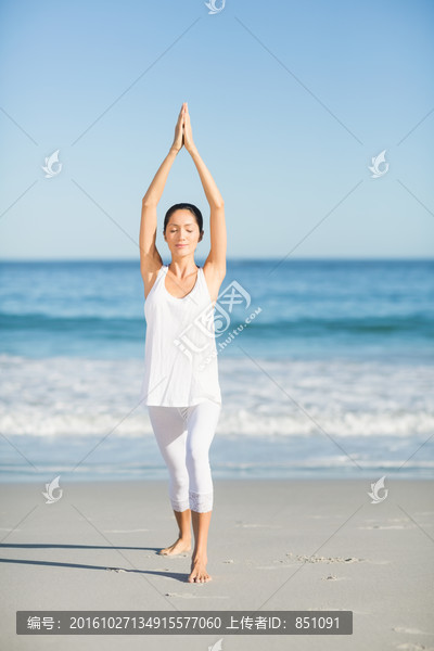年轻女人站在沙滩上做瑜伽