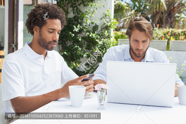 两个男人在咖啡店外用电脑和手机