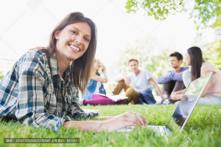 趴在草坪上使用电脑的女学生