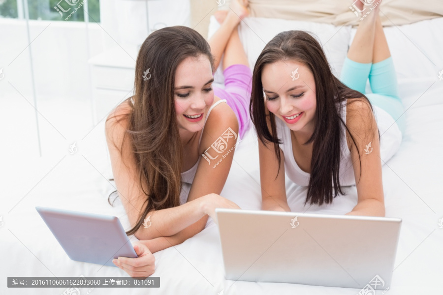 在床上使用电子设备的两个女人