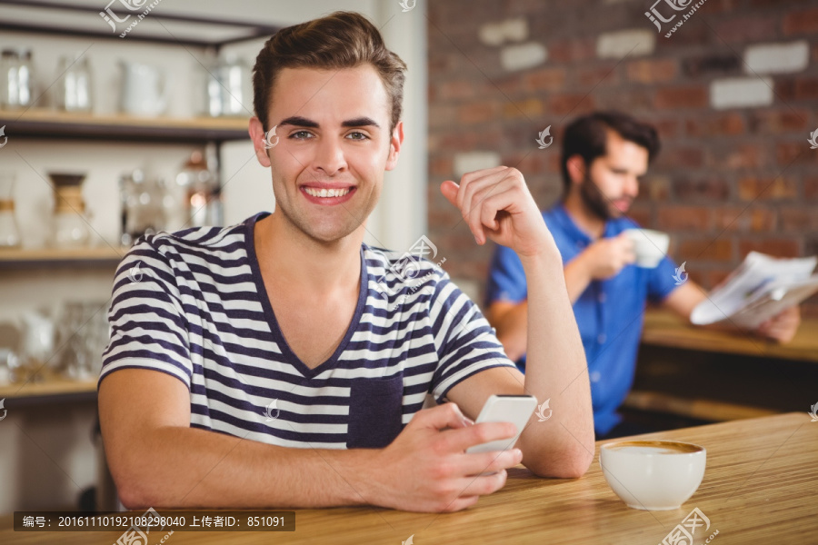微笑的男人在咖啡馆里使用手机