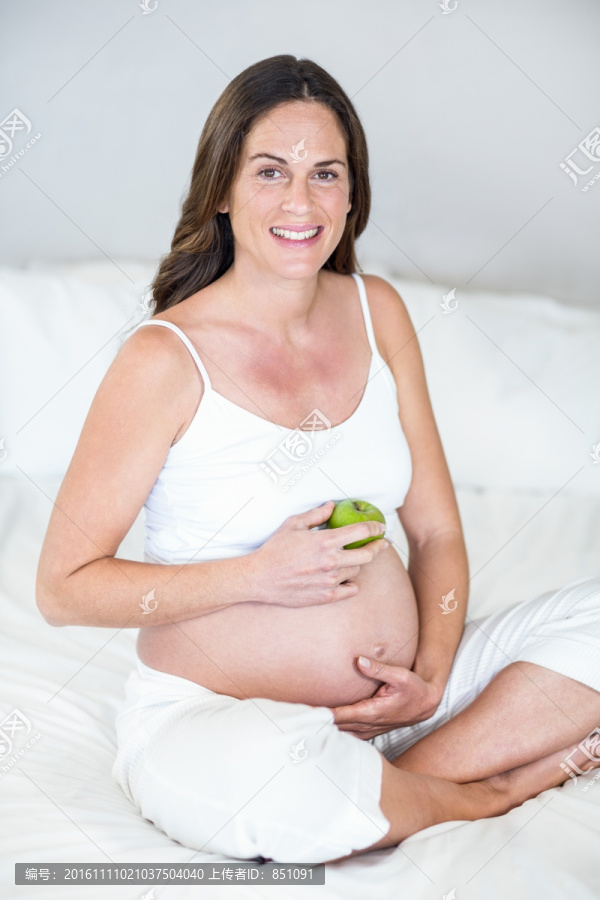 拿着苹果坐在床上的孕妇