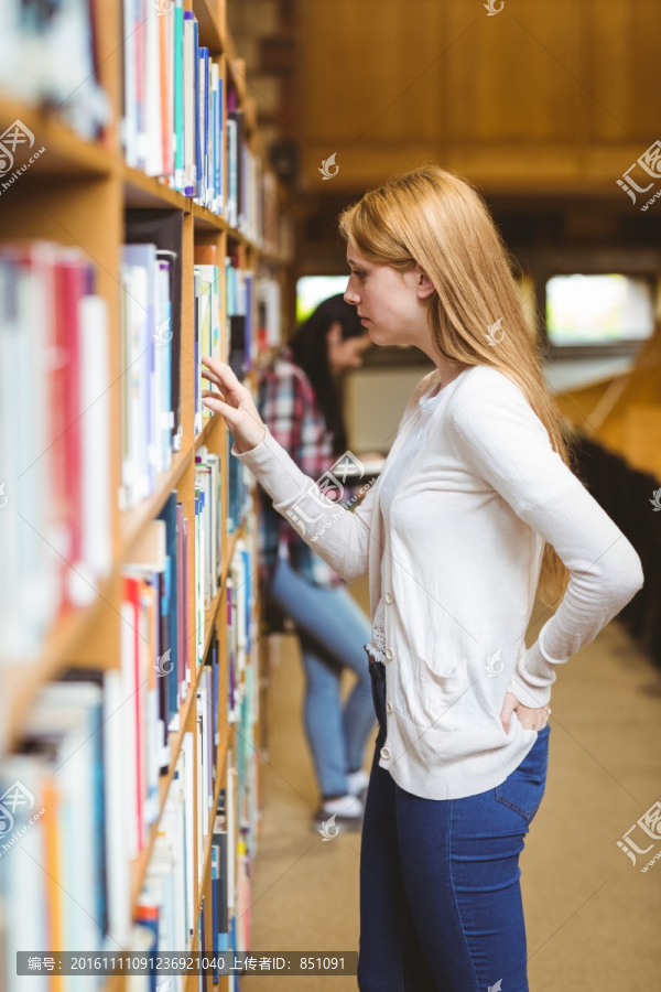 金发学生在大学图书馆书架上找书