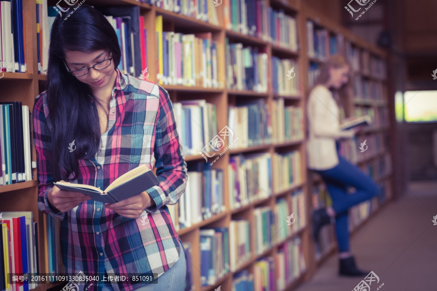 微笑的学生靠在书架上看书