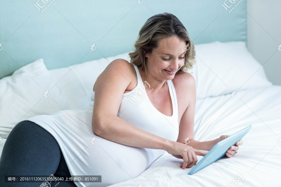 躺在床上使用平板电脑的孕妇