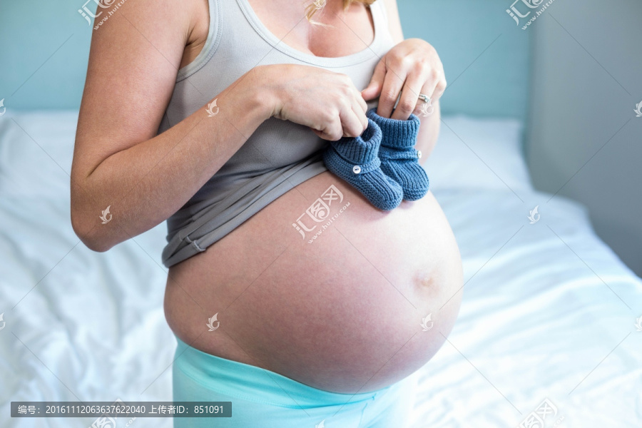 拿着一双小鞋放在肚子上的孕妇