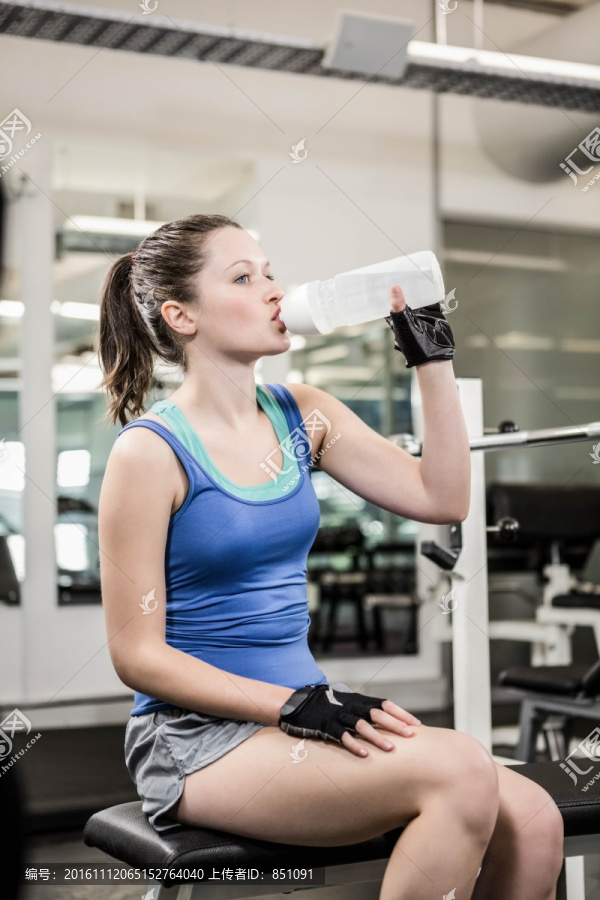 在健身房里喝水的年轻女人