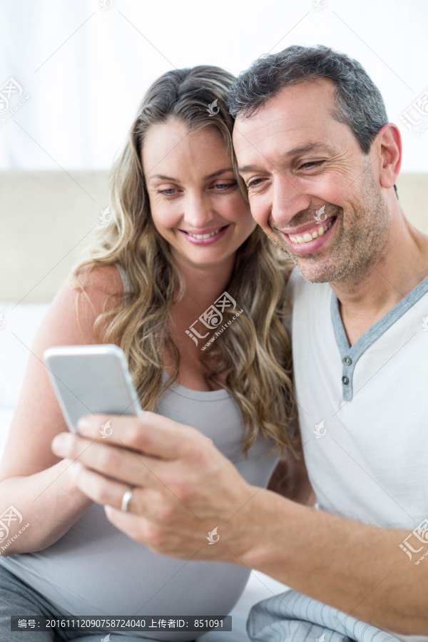 坐在床上使用手机的一对夫妇