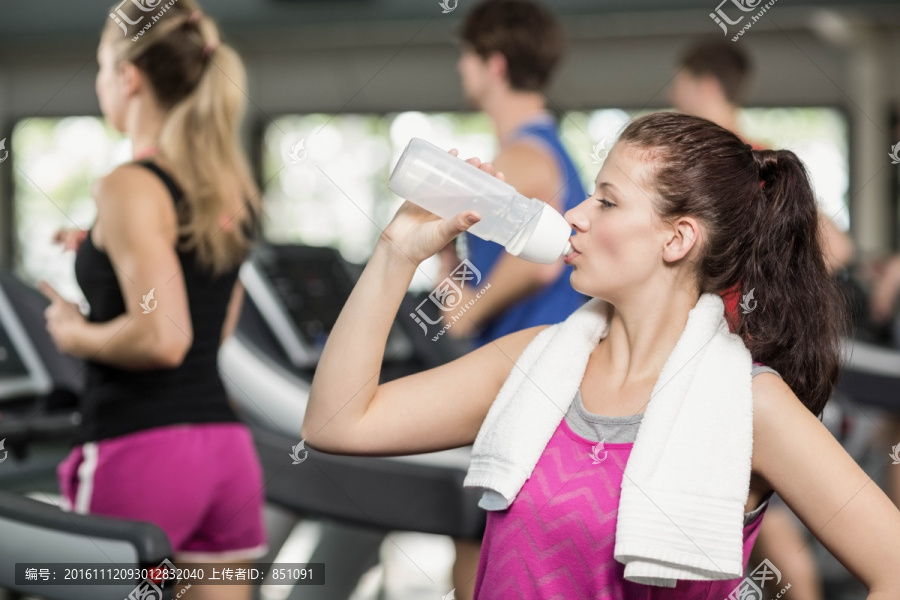 在健身房里喝水的年轻女人