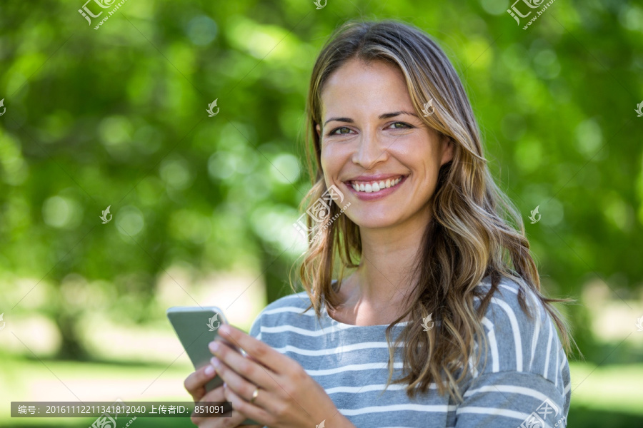 微笑的女人在公园里使用手机