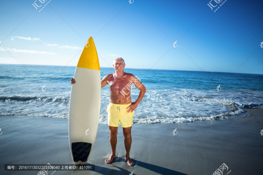 拿着冲浪板站在海滩上的老人