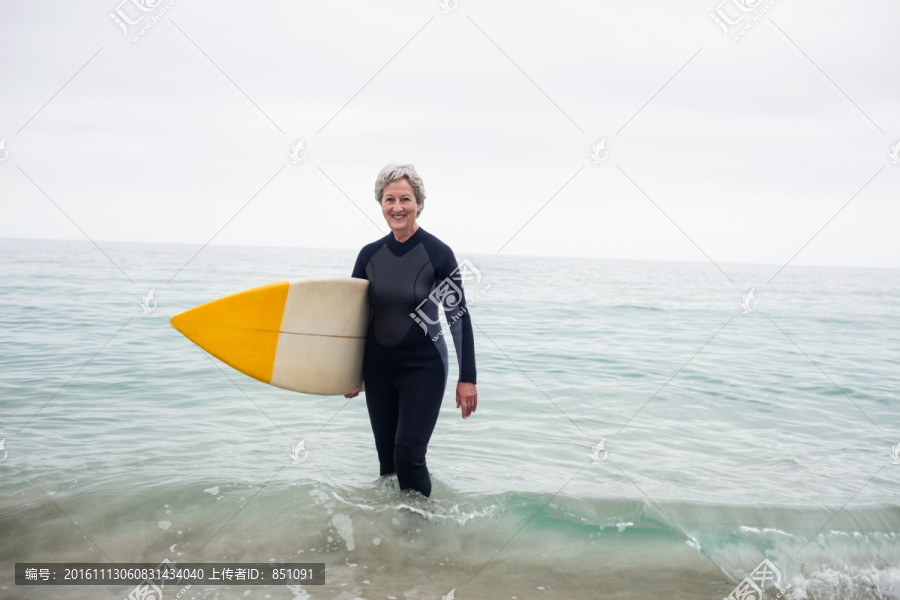 拿着冲浪板站在海水里的老太太