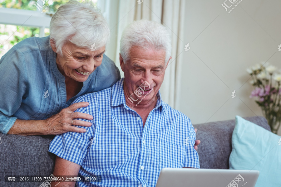 在客厅里使用笔记本电脑的老夫妇
