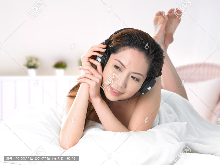 趴在床上戴着耳机听音乐的女人