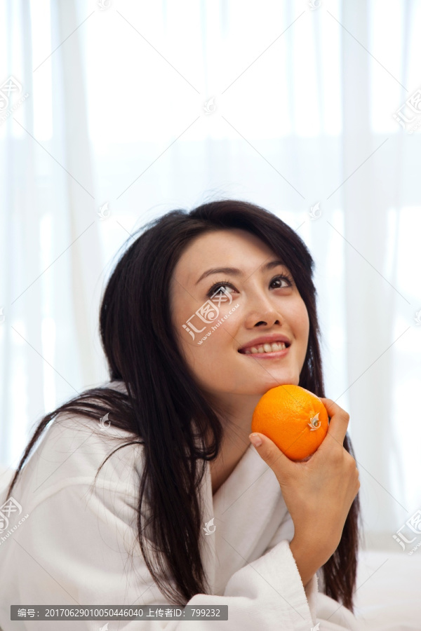 穿浴袍的年轻女人拿着橙子