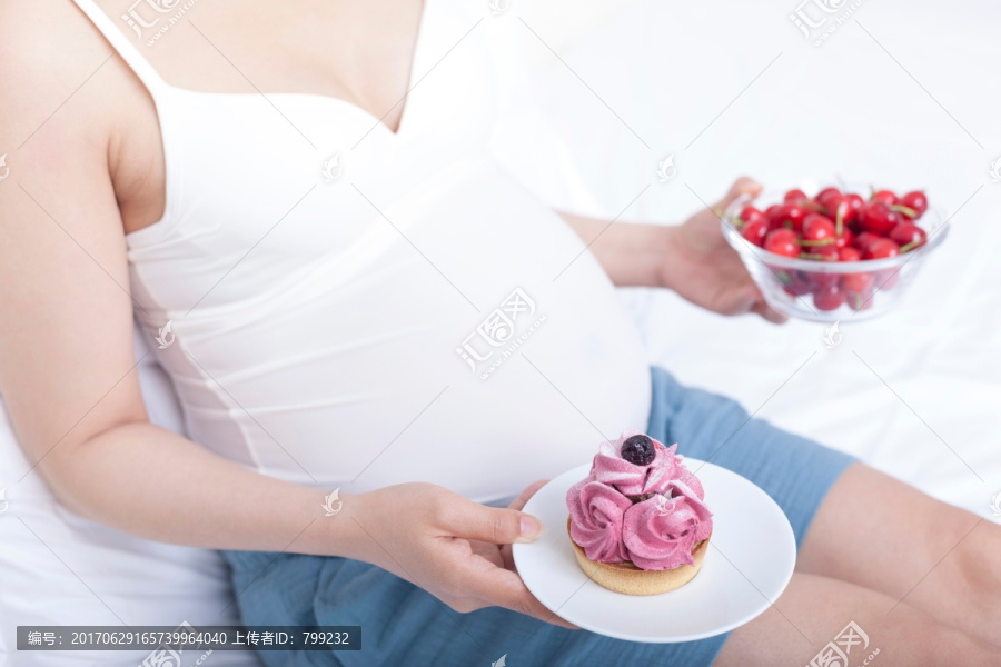 孕妇坐在床上拿着水果和蛋糕