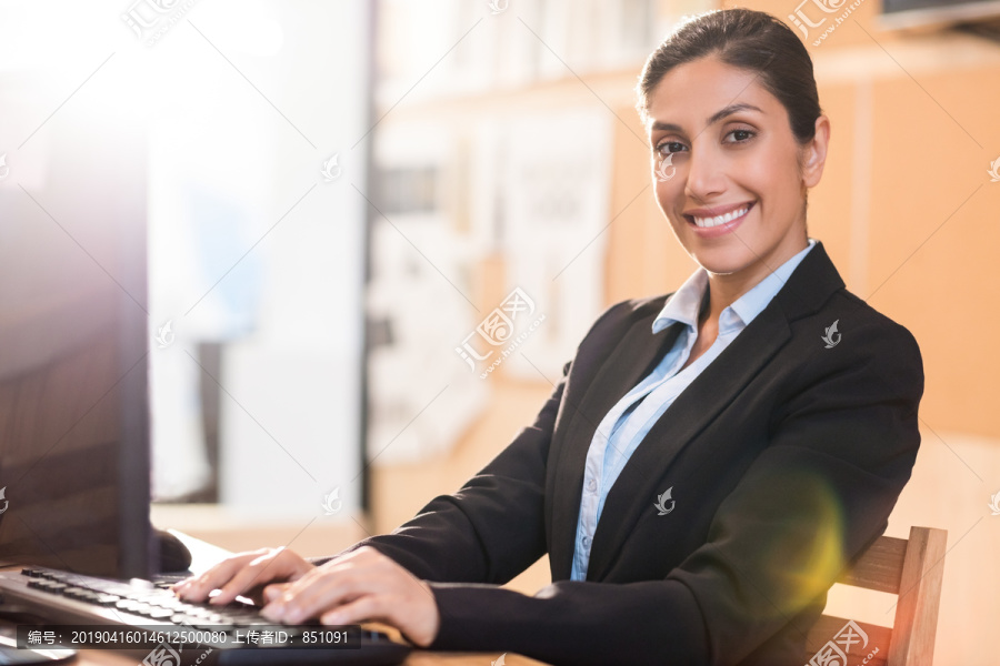 微笑的女商人在办公室键盘上打字