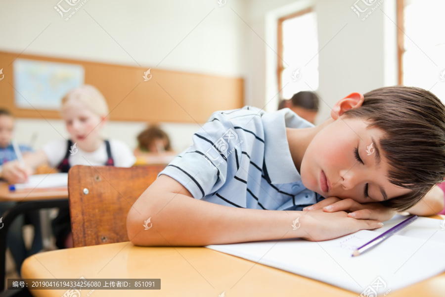 疲倦的小学生在书桌旁休息