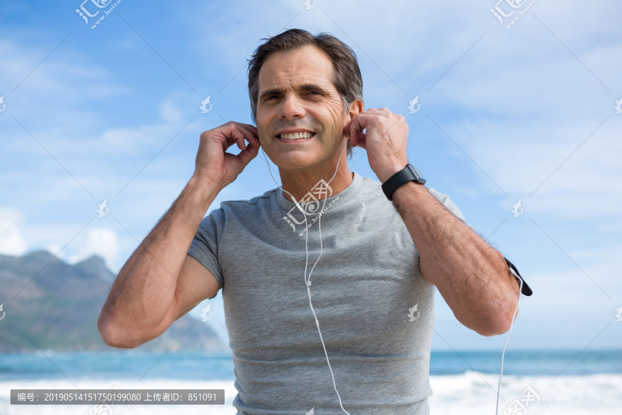 微笑的男人在海滩上用耳机听音乐