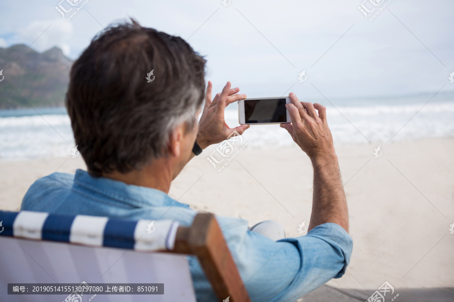 沙滩上用手机拍摄的男子