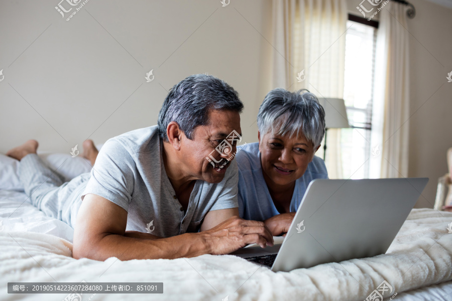 在卧室里用笔记本电脑的老夫妇