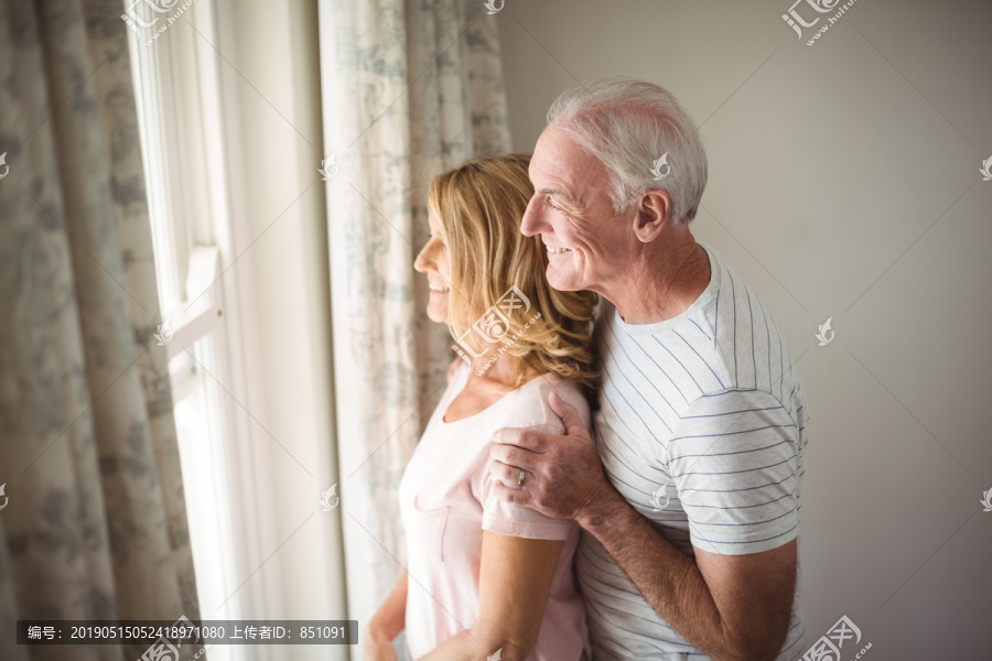 一对幸福的老年夫妇站在家里窗户