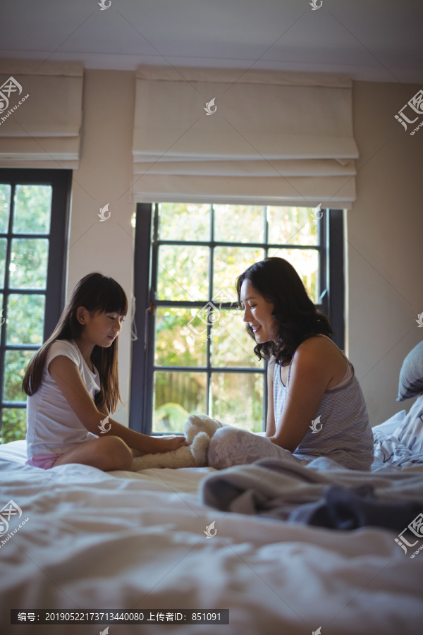 女儿和母亲在卧室里玩泰迪熊