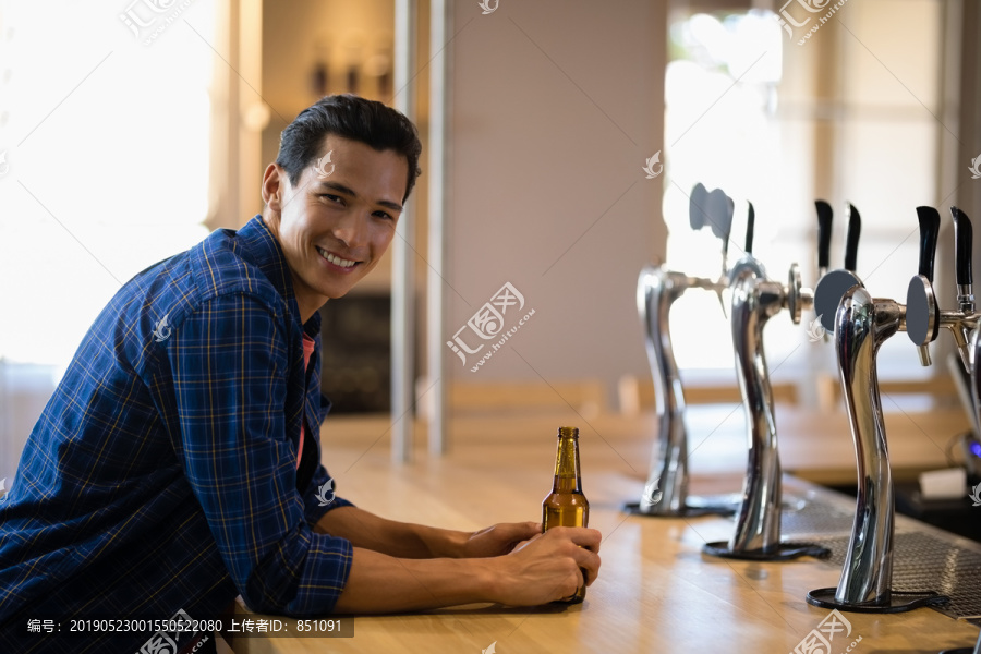 酒吧柜台上喝啤酒的男人的画像