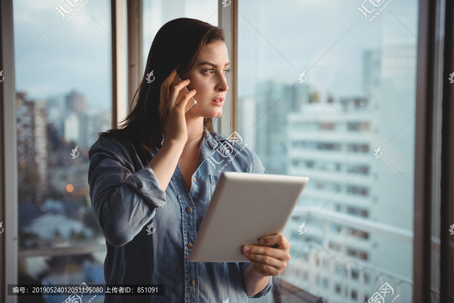 女人在家拿着电脑一边用手机说话