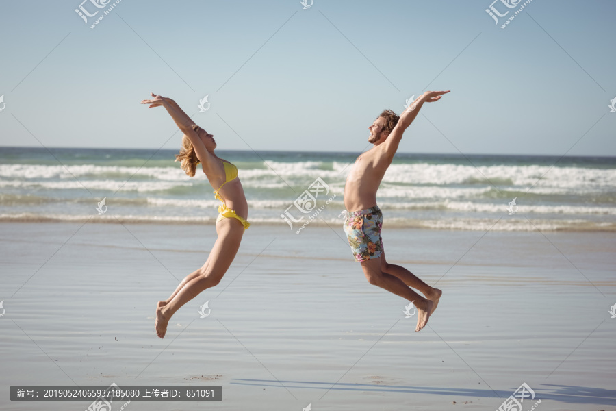快乐夫妻在海滩上跳跃的侧视图