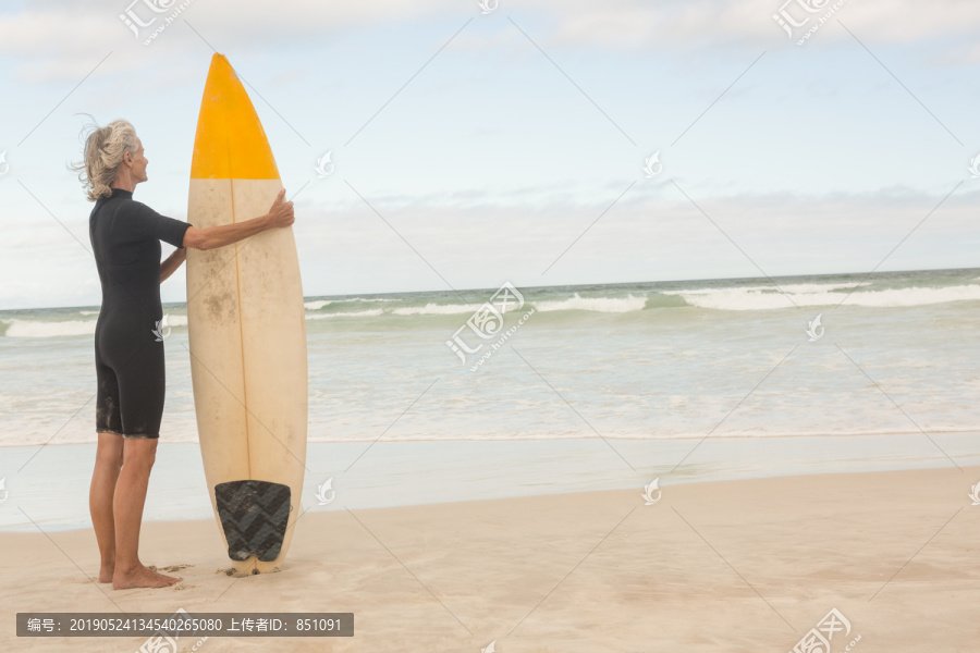 站在沙滩上拿冲浪板的老妇人