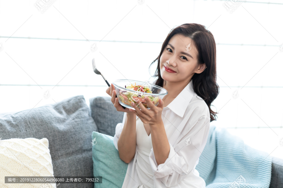 年轻女子坐在沙发上吃色拉