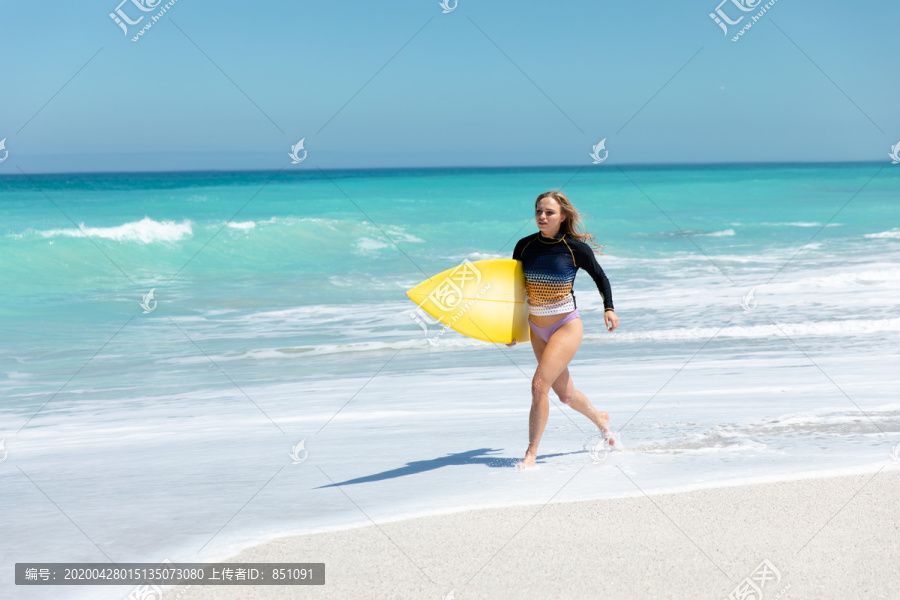 妇女拿着冲浪板在海滩上漫步