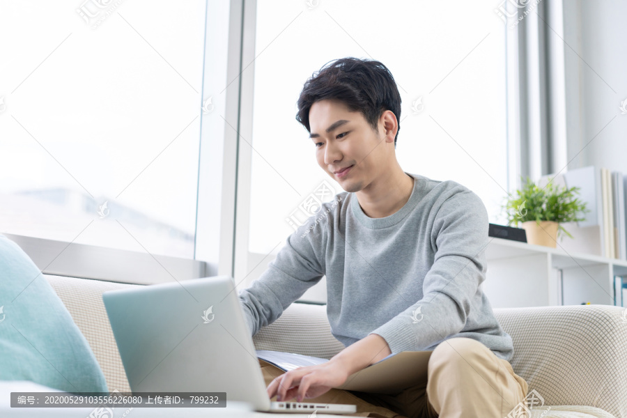 年轻男子在沙发上使用笔记本电脑