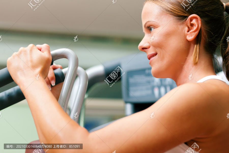在健身房里，一个女子在蝶泳机上进行举重健身训练