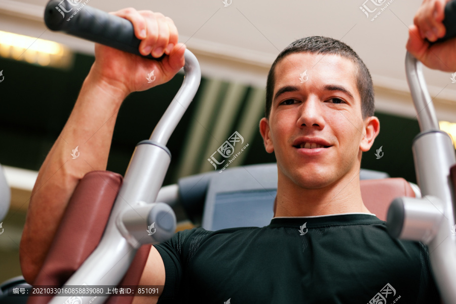 在健身房里，男子在蝶泳机上进行举重健身训练